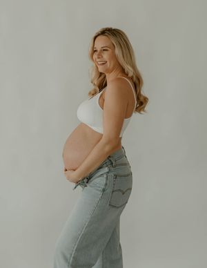 Side view of pregnant woman in casual denim and white top smiling against neutral background at a studio in Huntington Beach