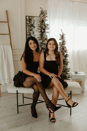 Group wearing stylish black outfits poses on bench in minimalist white studio setting.