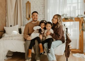 Family poses together in cozy indoor setting with white brick walls and natural lighting.