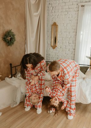 Family in matching plaid Christmas pajamas poses creatively on hardwood floor.