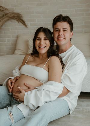 Candid maternity portrait with couple in white and denim sitting on couch at a studio in Huntington Beach