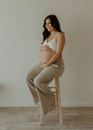 Natural maternity portrait of pregnant woman in neutral tones sitting on wooden stool at a studio in Huntington Beach