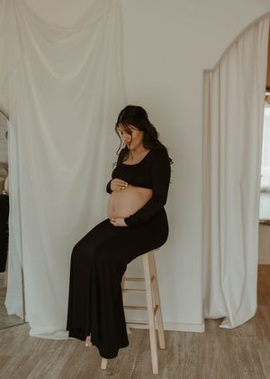 Minimalist maternity portrait of pregnant woman in black dress against white backdrop at a studio in Huntington Beach