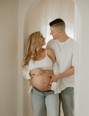 Indoor maternity photo of couple in casual white and denim sharing tender moment in doorway at a studio in Huntington Beach