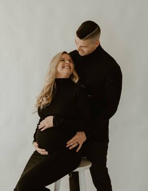 Intimate maternity photoshoot of couple in black outfits against white backdrop at a studio in Huntington Beach