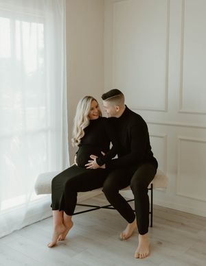 Romantic maternity portrait of couple sitting together in black clothing by window at a studio in Huntington Beach