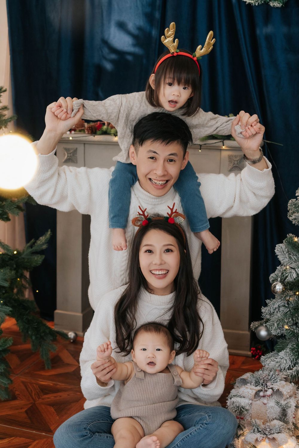 Happy Asian family in matching sweaters with reindeer antlers celebrating Christmas with two young children.