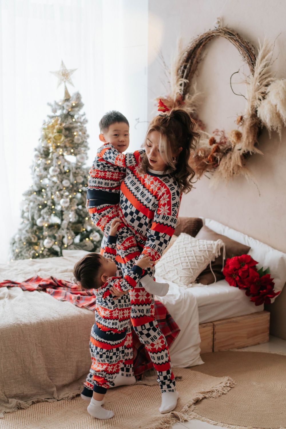 Two people in matching holiday pajamas dance playfully in front of a decorated Christmas tree.