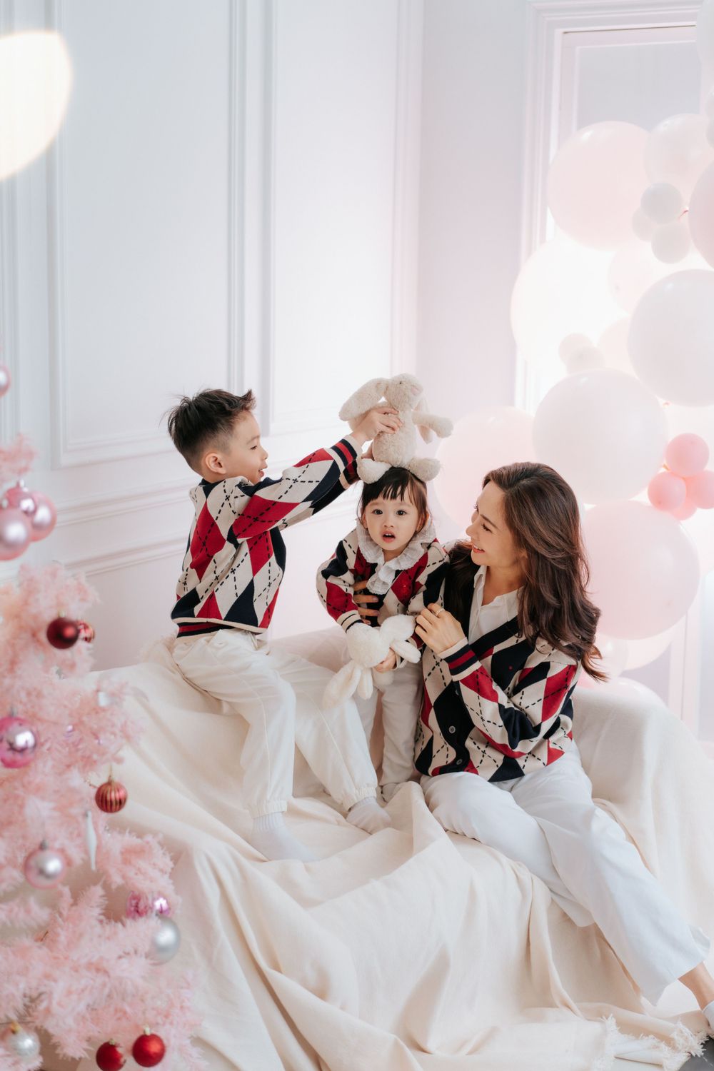 Family enjoying playful moment on white bedding near pink Christmas tree with matching outfits.