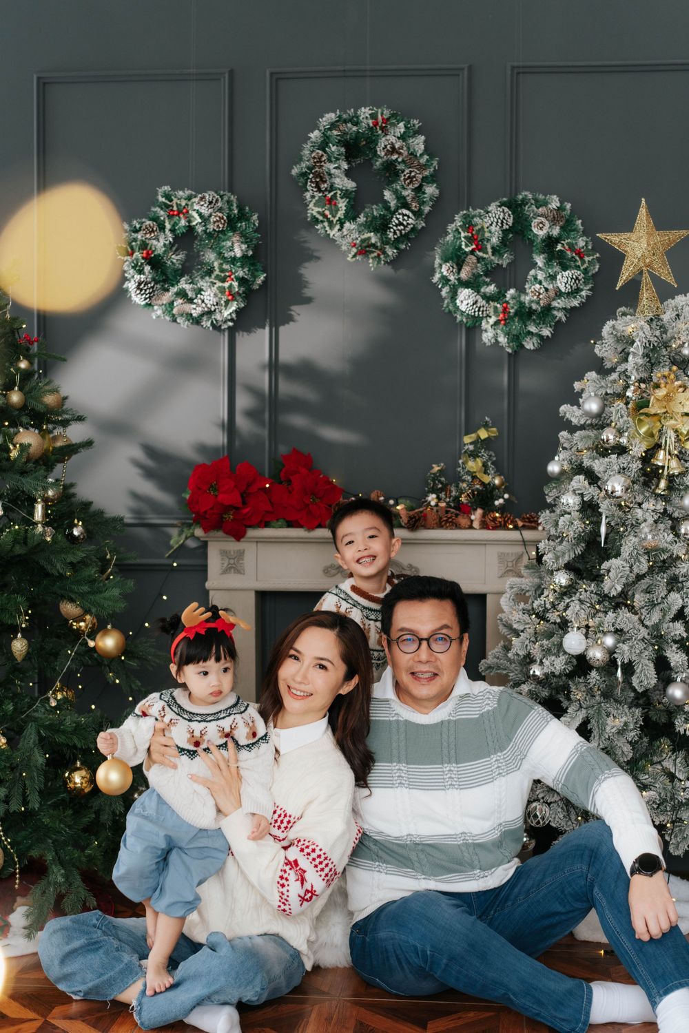Family holiday portrait with Christmas trees, wreaths, and festive decorations.