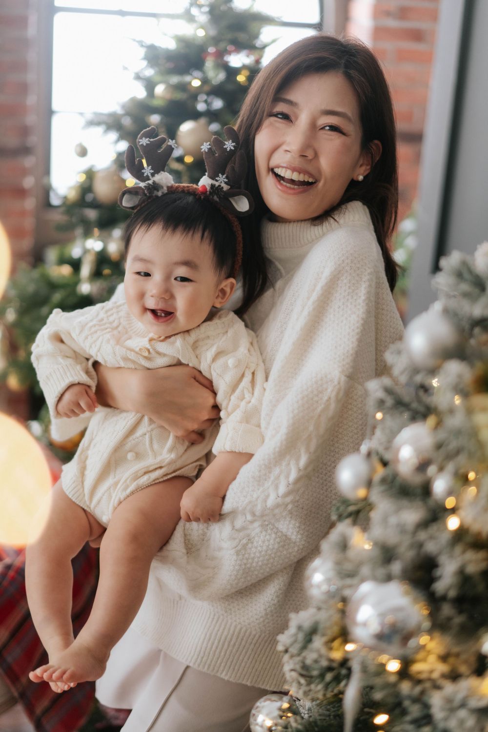 Joyful holiday portrait in front of Christmas tree with decorative lights and ornaments.