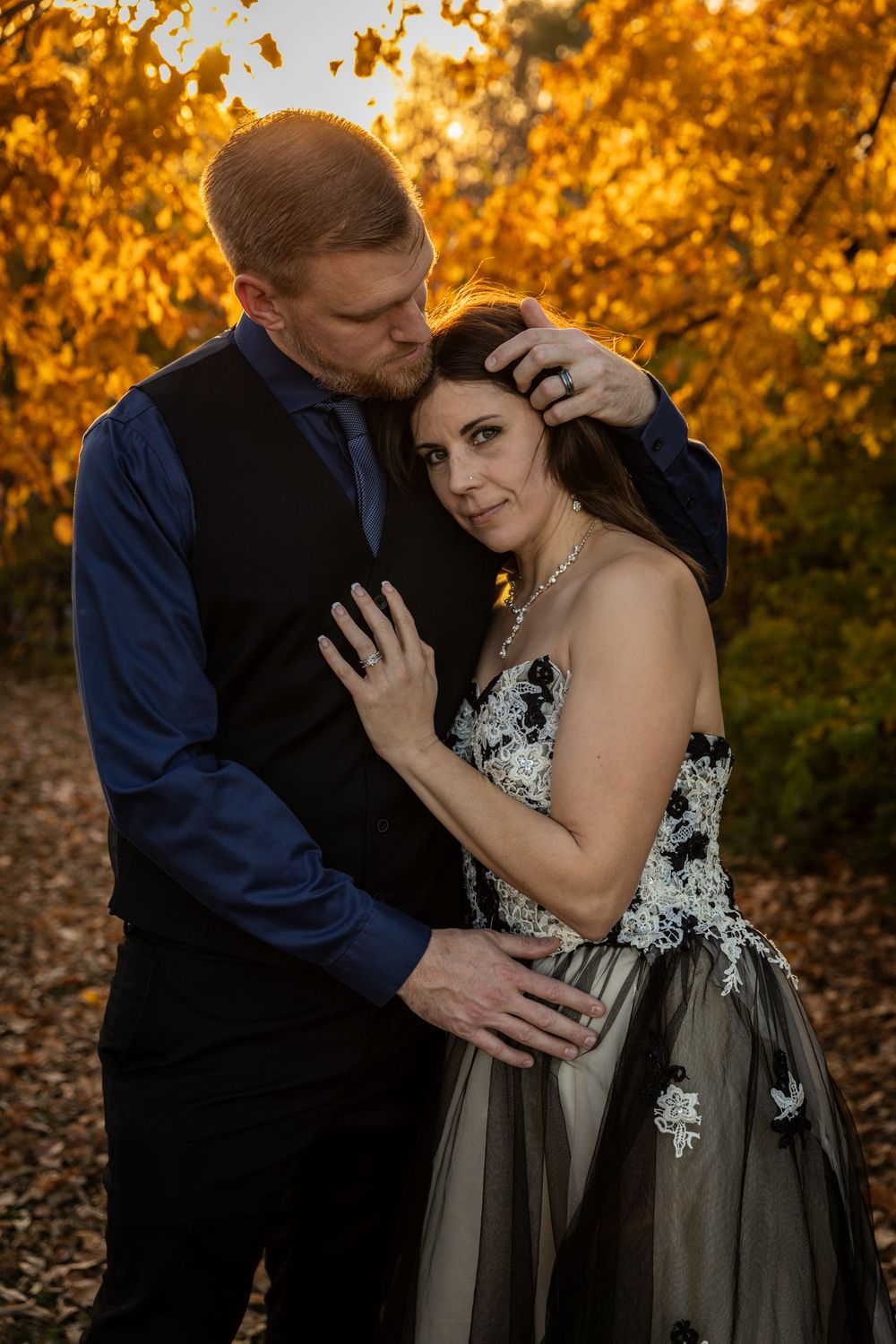 A couple shares an intimate moment at sunset among golden autumn foliage, with the bride wearing a black and white gown.
