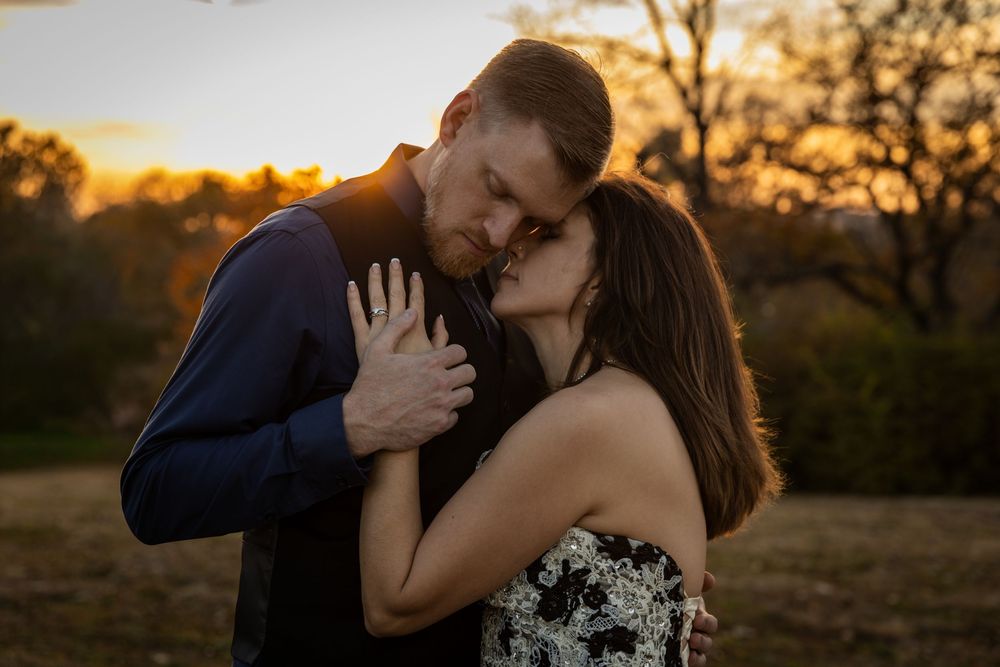 A romantic couple embraces during golden hour sunset in a natural outdoor setting.