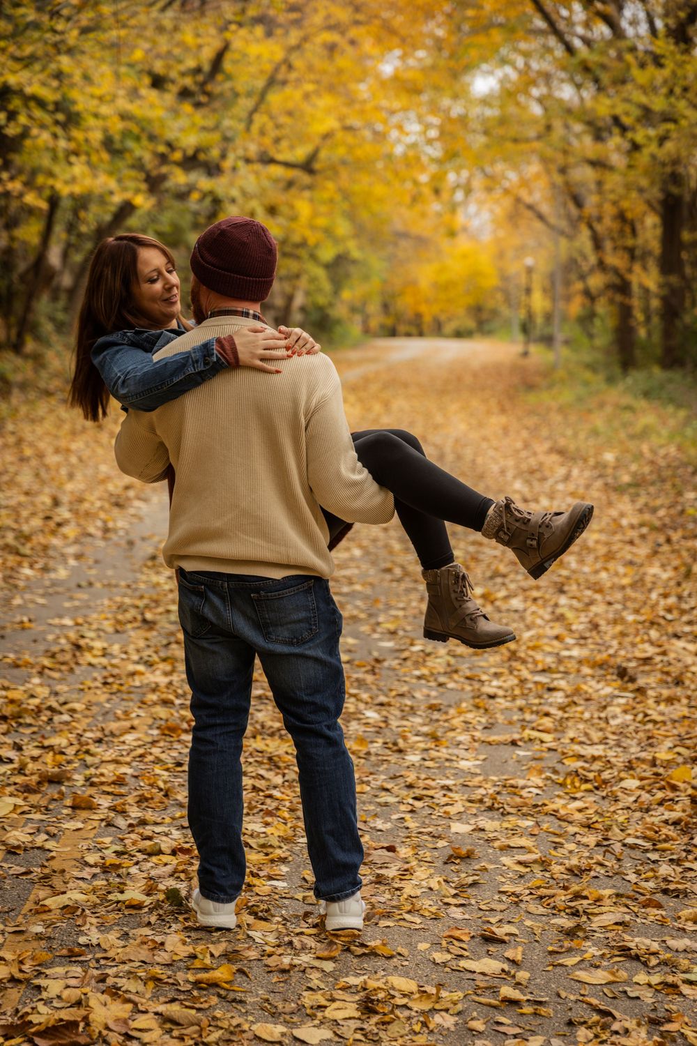 A couple shares a romantic moment on a leaf-covered path surrounded by golden autumn foliage in the forest.