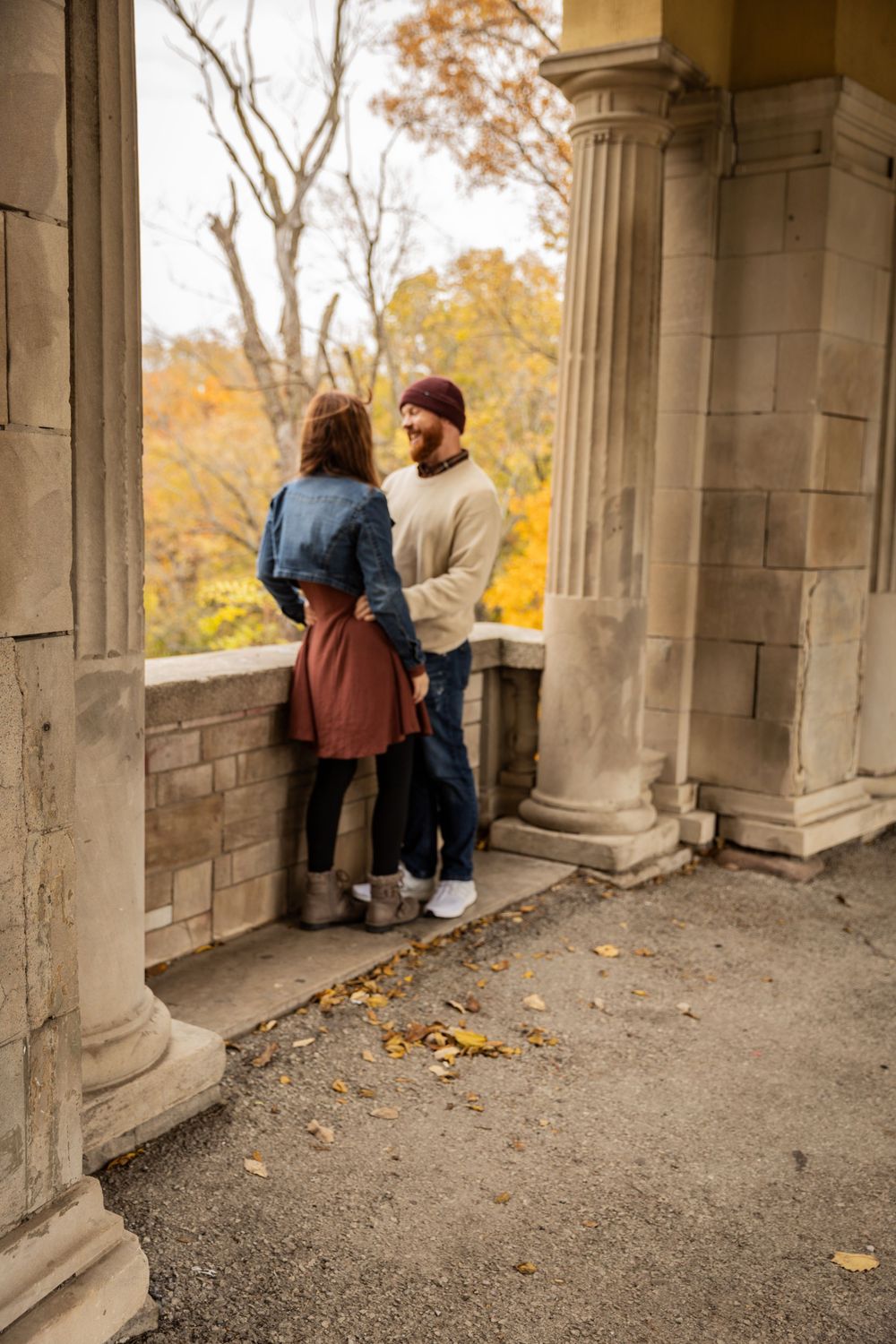 People admire autumn foliage through stone archways at a historic overlook on a fall day.