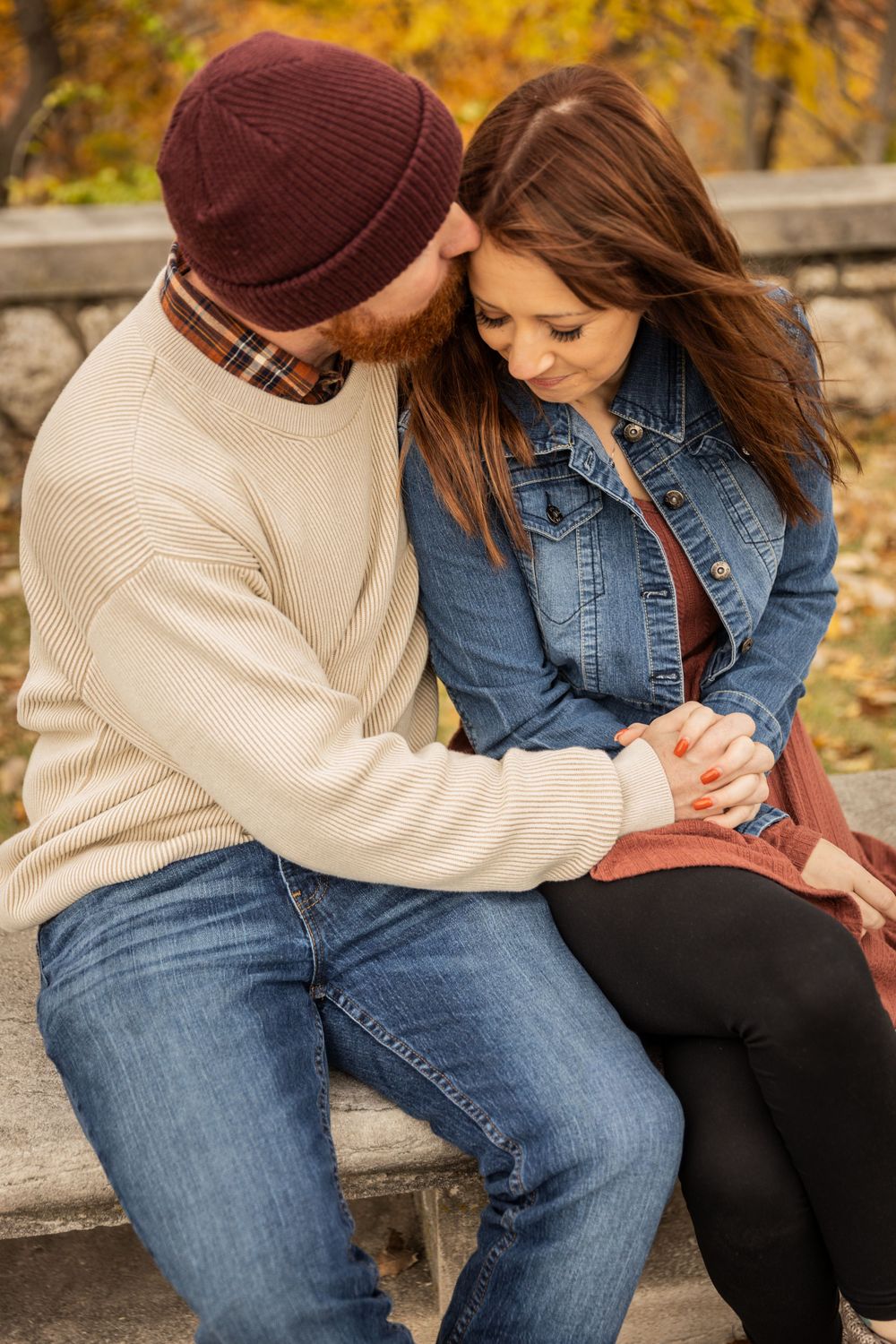 Romantic autumn couple sitting close together on stone steps with fall foliage in background.