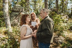 Couple exchanges wedding vows outdoors in forest with person in Bigfoot costume officiating the rustic woodland ceremony.