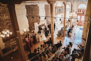 Wedding ceremony in historic brick venue with exposed beams and arched windows.