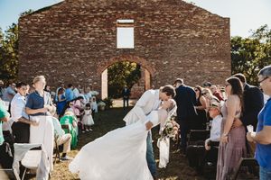 Bride and groom share a romantic dip kiss while walking down the aisle at an outdoor rustic brick chapel wedding.