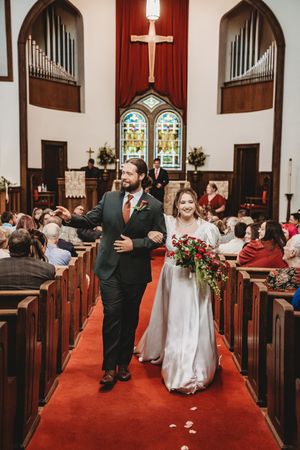 Bride and groom walk down red carpet aisle in a traditional church after wedding ceremony.
