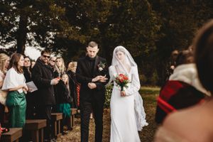 Wedding ceremony guests gather outdoors under string lights and autumn trees.