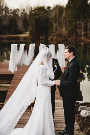 Wedding couple shares intimate moments on a wooden dock by a serene lake.
