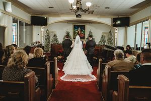 Bride walks down church aisle in elegant white gown with long veil during Christmas wedding ceremony.