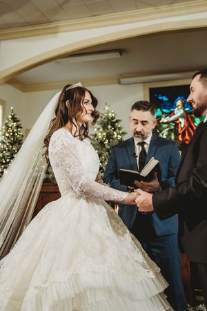 Bride and groom exchange vows at a Christmas church wedding ceremony, officiated by a minister holding a book.