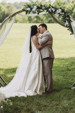 Romantic outdoor wedding ceremony moment under a floral arch with white fabric draping.