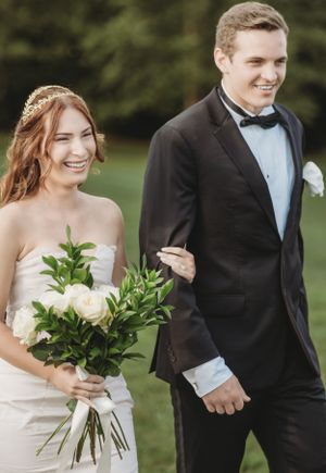 Wedding couple shares joyful moments while holding white floral bouquet outdoors.