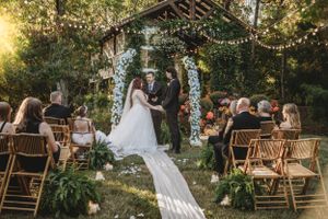Outdoor wedding ceremony setup with wooden chairs and string lights at sunset.