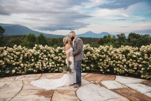 Panoramic view of mountain wedding venue with stone patio and flowering bushes.