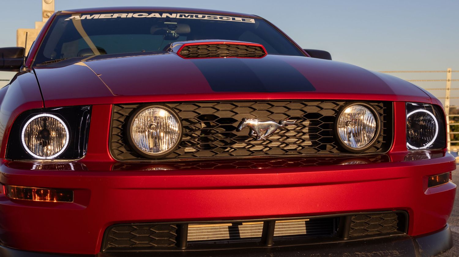 Close-up of red Ford Mustang front grille and headlights against bright sky.