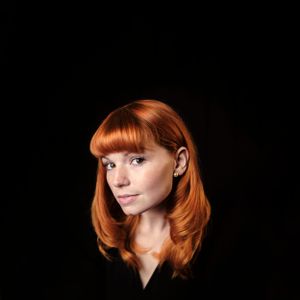 Headshot of a red haired lady, She is in a black top and has a black background. taken near Hereford in Herefordshire.