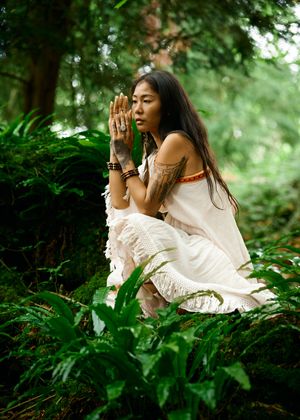 outdoor boudoir photo in the forest of dean, showing a woman in a light flowing dress sitting among the green ferns.