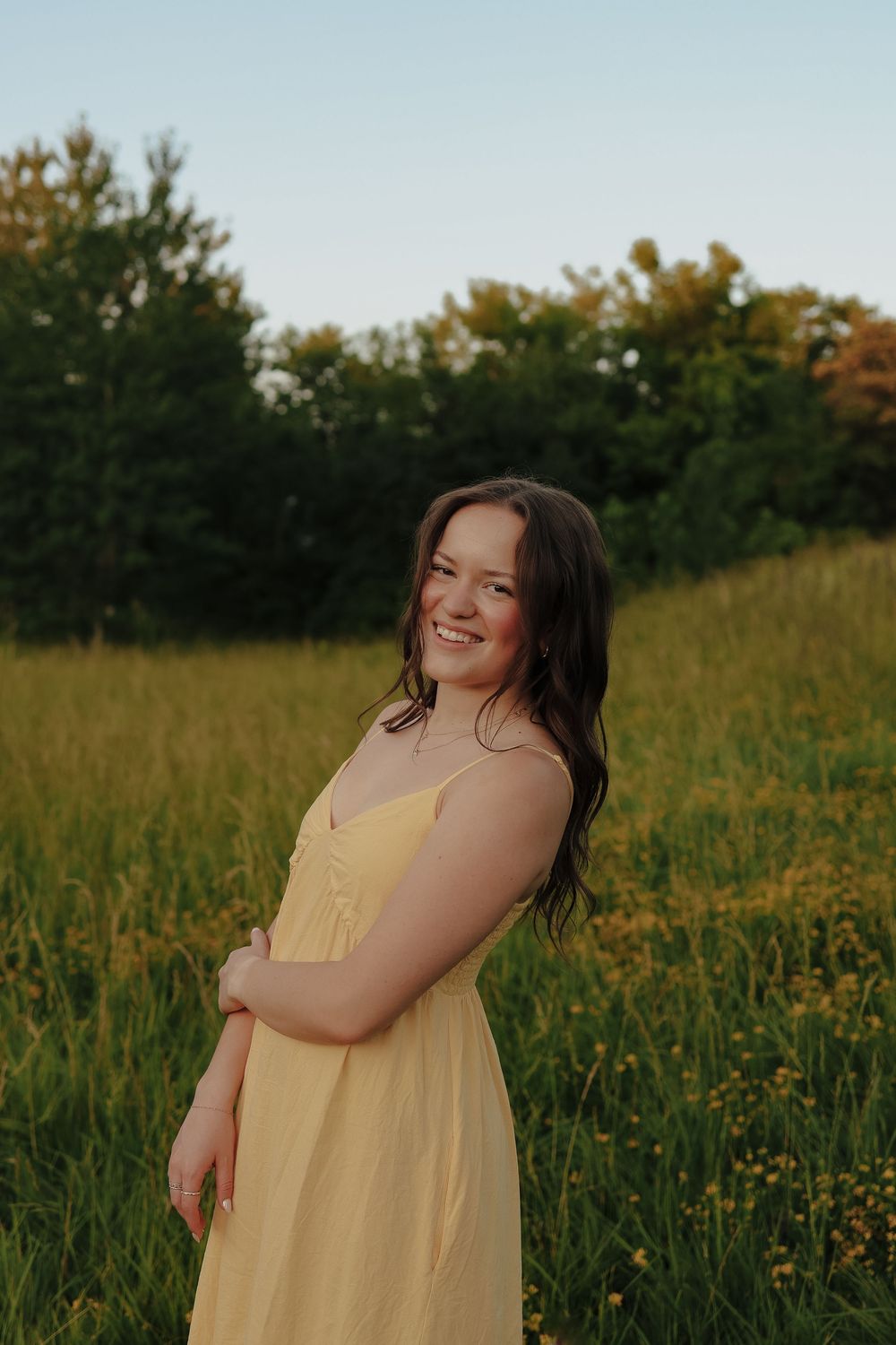 A person wearing a yellow sundress poses joyfully in a sunny wildflower field during golden hour.