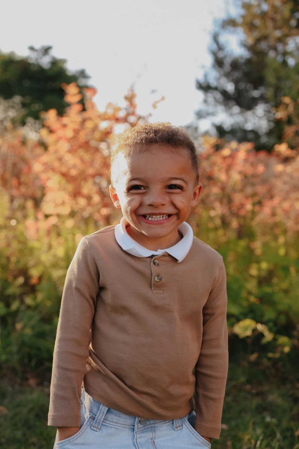 Three photos of a young child wearing a brown sweater and jeans smiling outdoors with autumn foliage in the background.