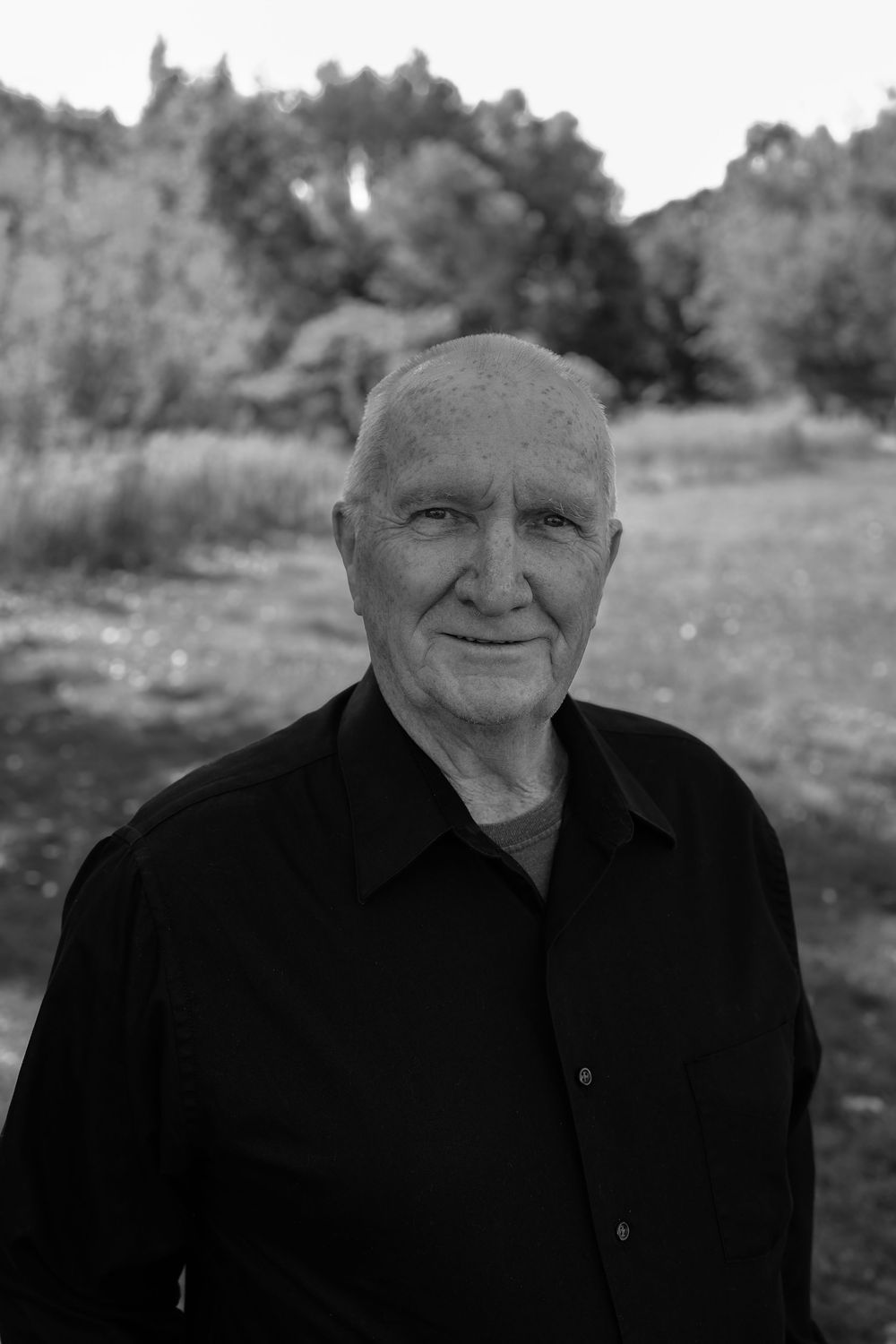 Black and white portrait series of an elderly person wearing dark clothing against a natural outdoor background.