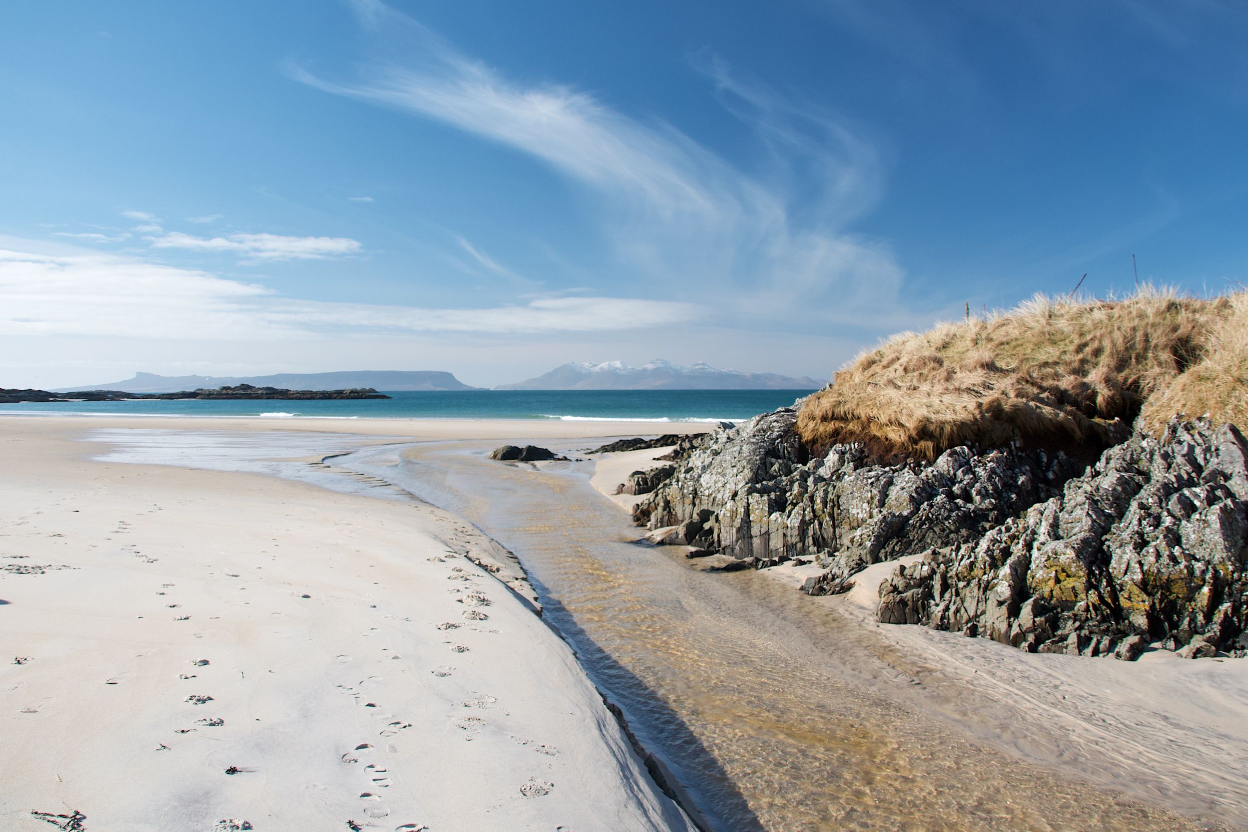 Panoramic coastal landscape showing sandy beach and rocky cliffs under blue skies.