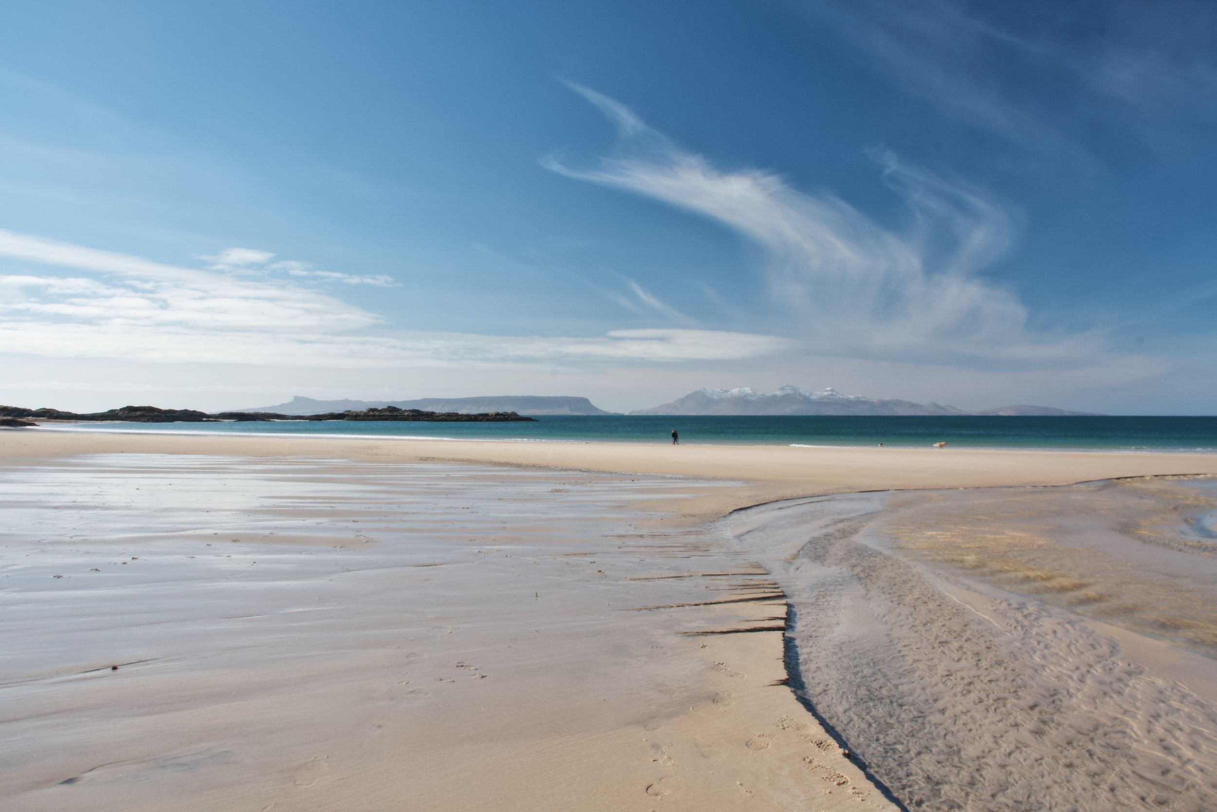 Panoramic view of a vast empty beach stretching along the coastline under a bright blue sky.