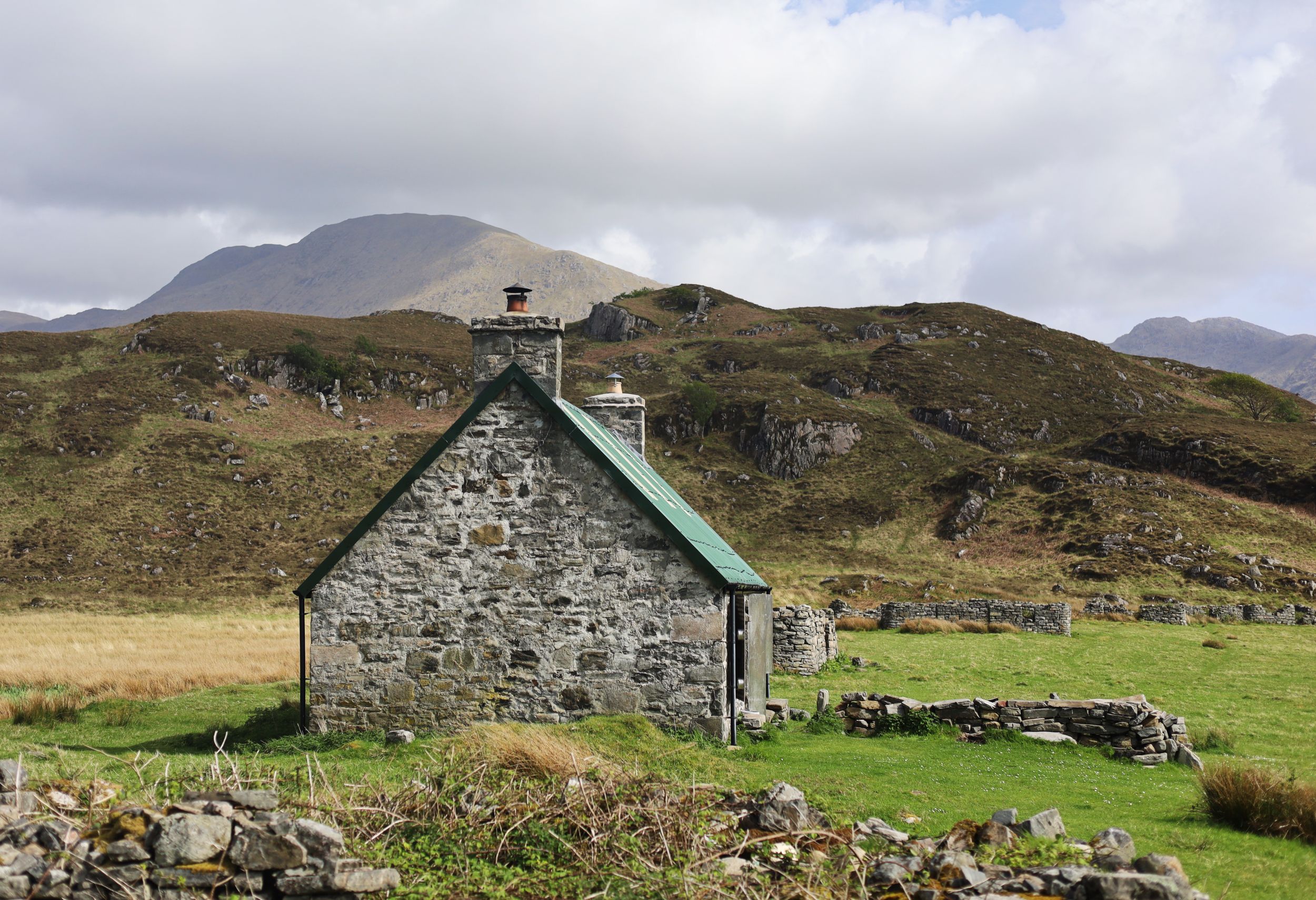 Traditional stone cottage with green roof nestled in the Scottish Highland countryside.