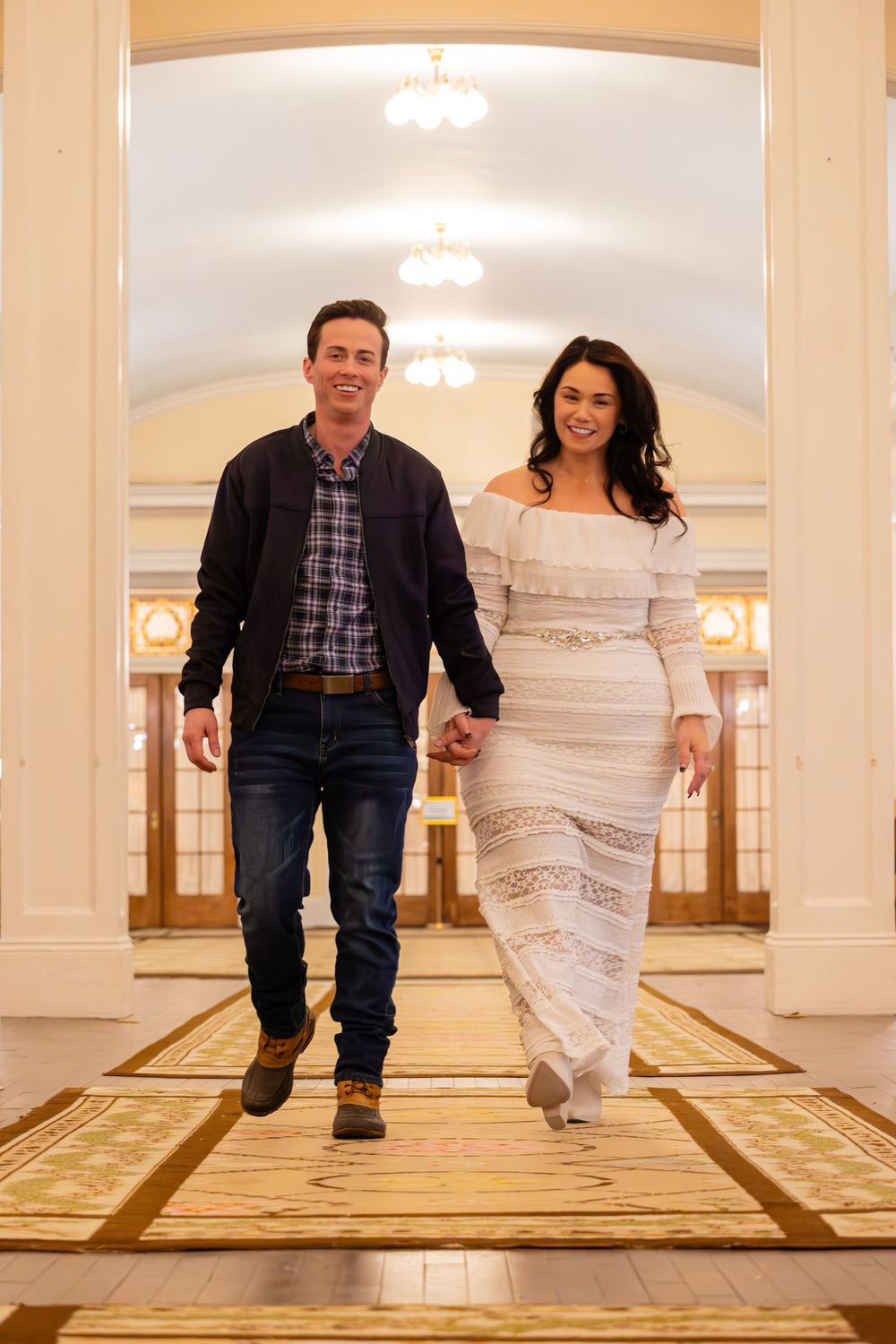 A couple walks together through an elegant hallway with chandeliers and ornate decor.