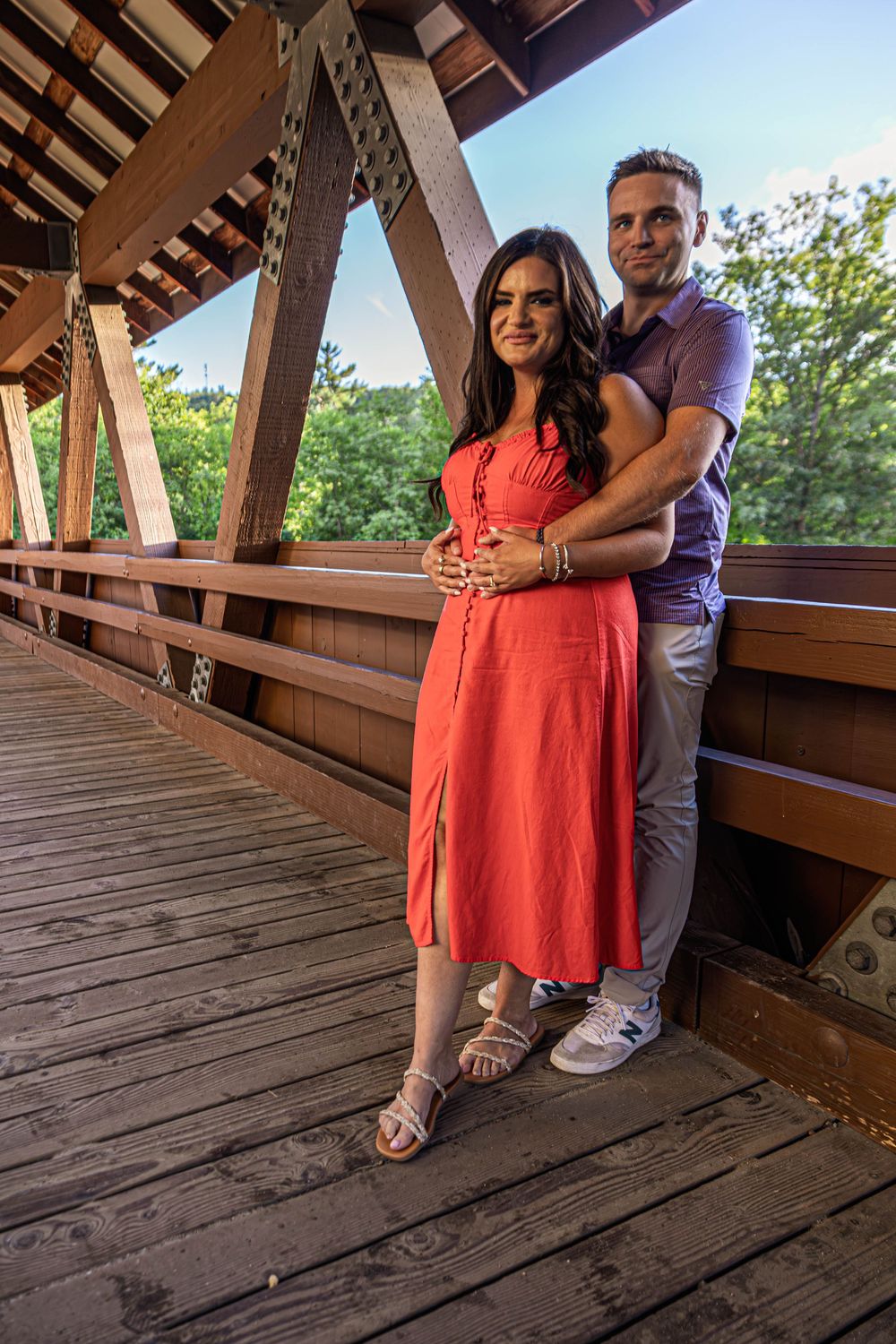 Couple embracing on a wooden covered bridge deck during a sunny afternoon.
