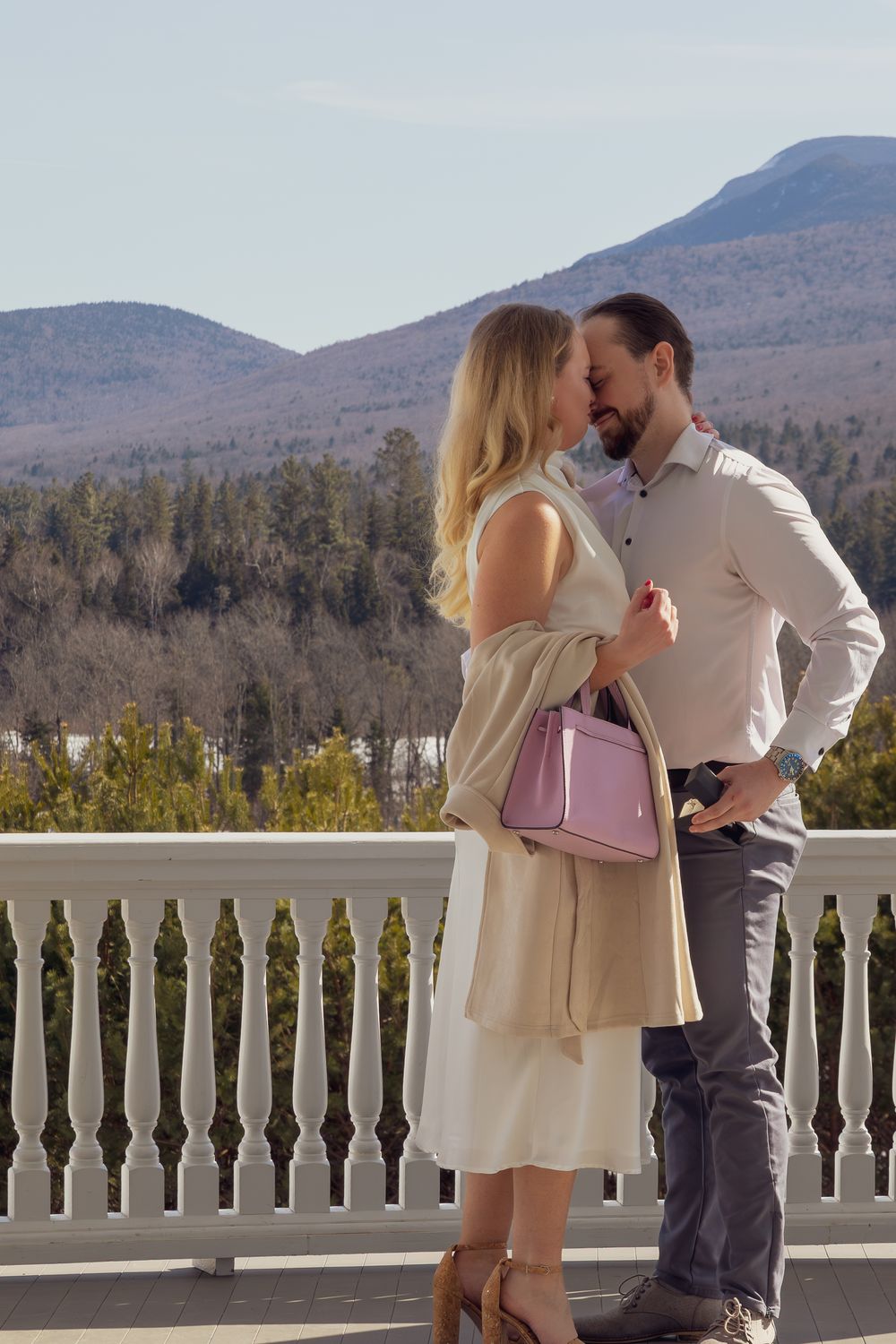 A couple shares romantic moments on a white-railed balcony with mountain views.