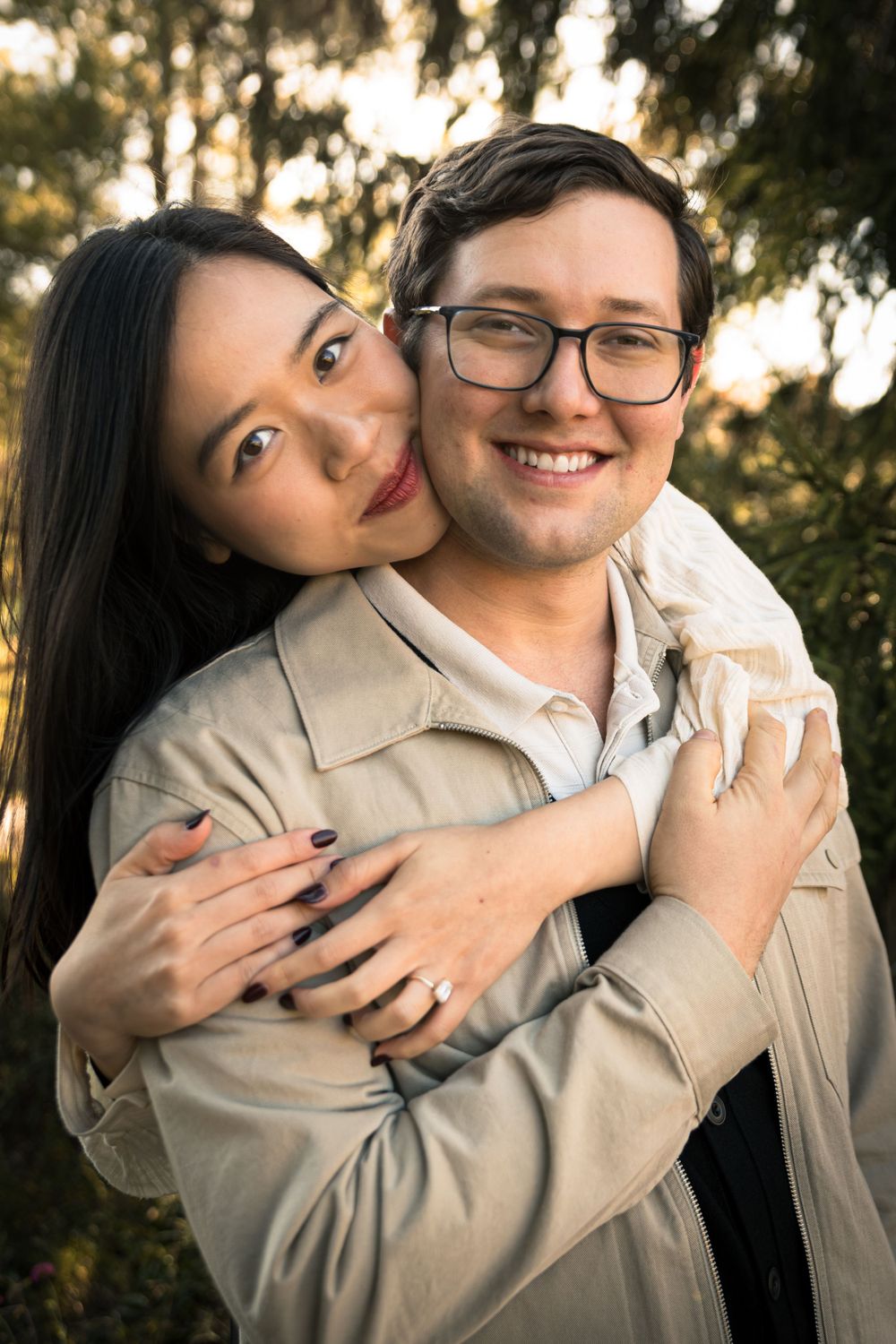 Couple embraces in warm sunlight with trees creating natural backdrop.