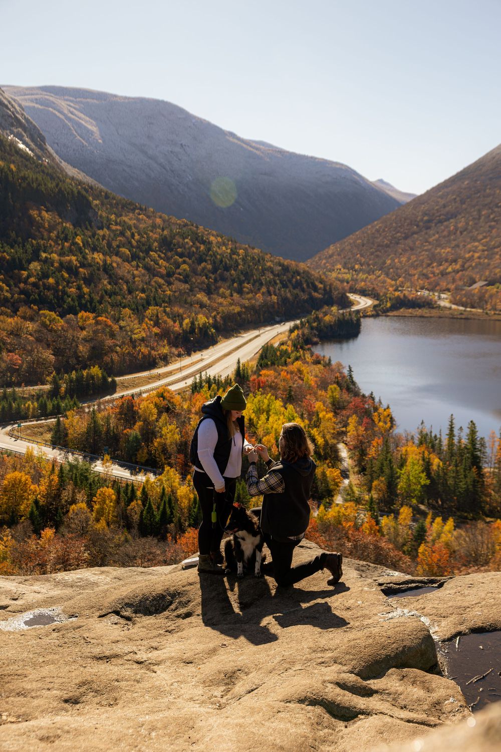 Couple sharing romantic proposal moment overlooking scenic mountain valley with fall foliage.