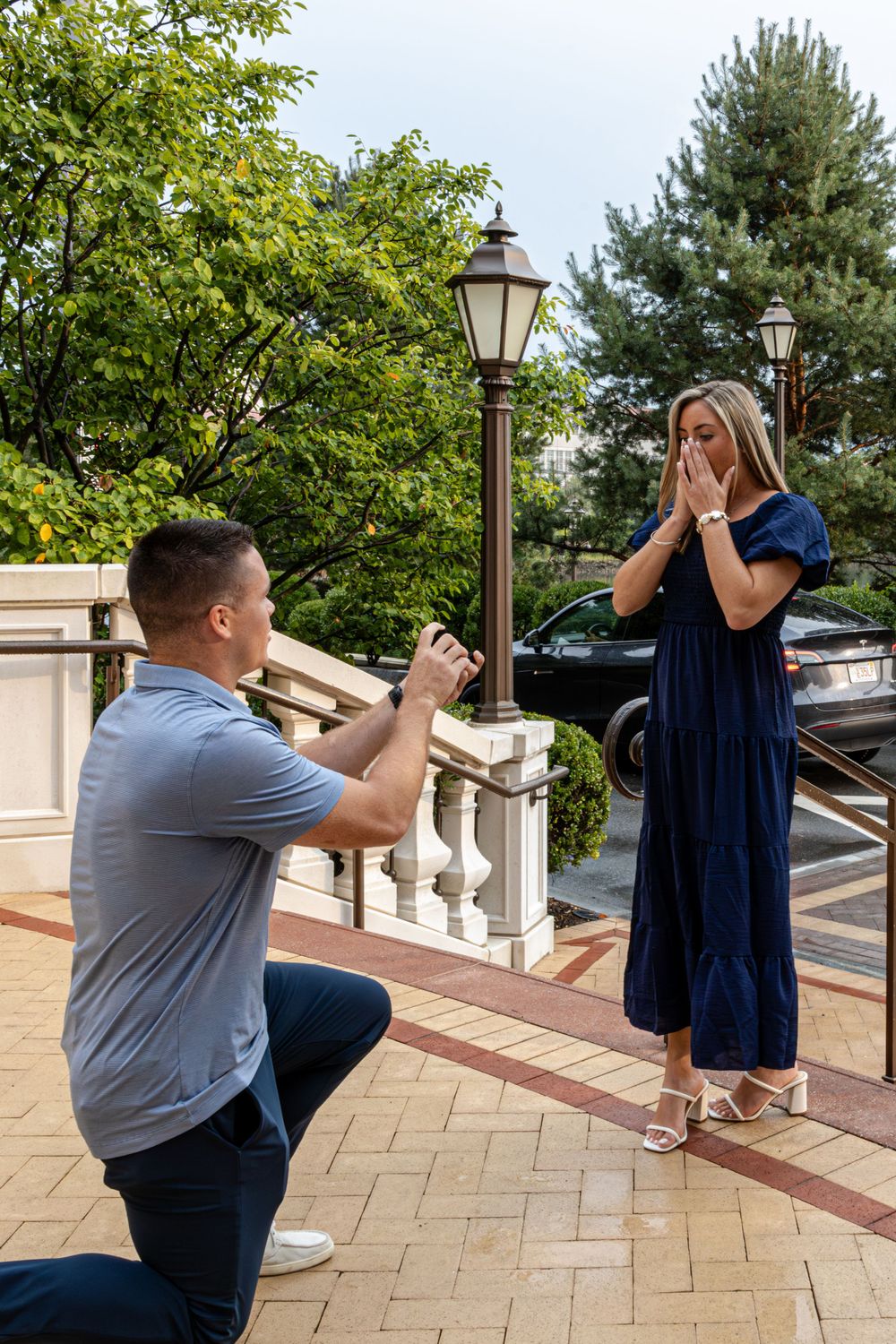 Couple poses on outdoor stone staircase with lampposts during engagement photoshoot.
