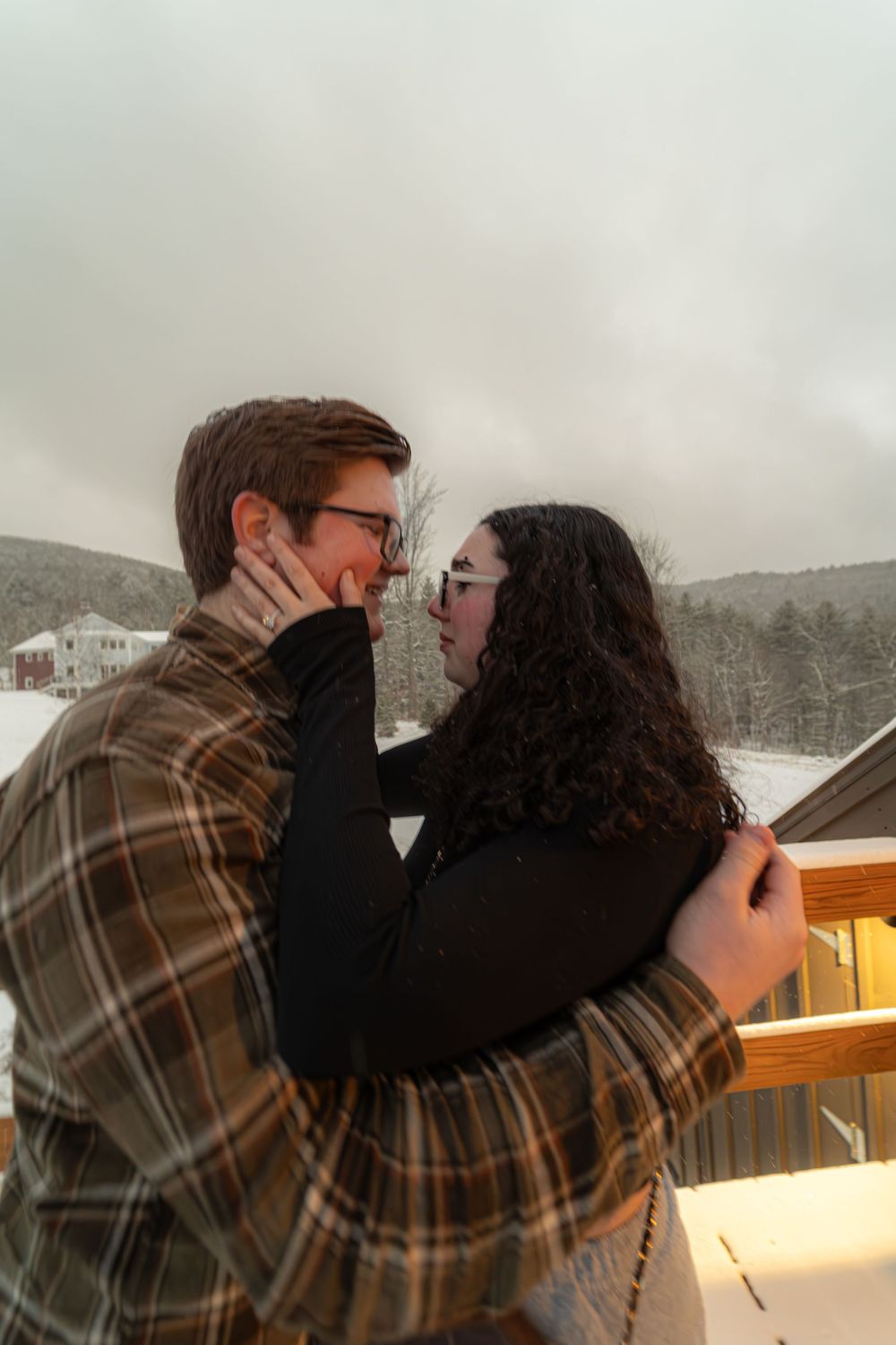 Romantic couple sharing intimate moments in a snowy winter setting with a cozy cabin in the background.