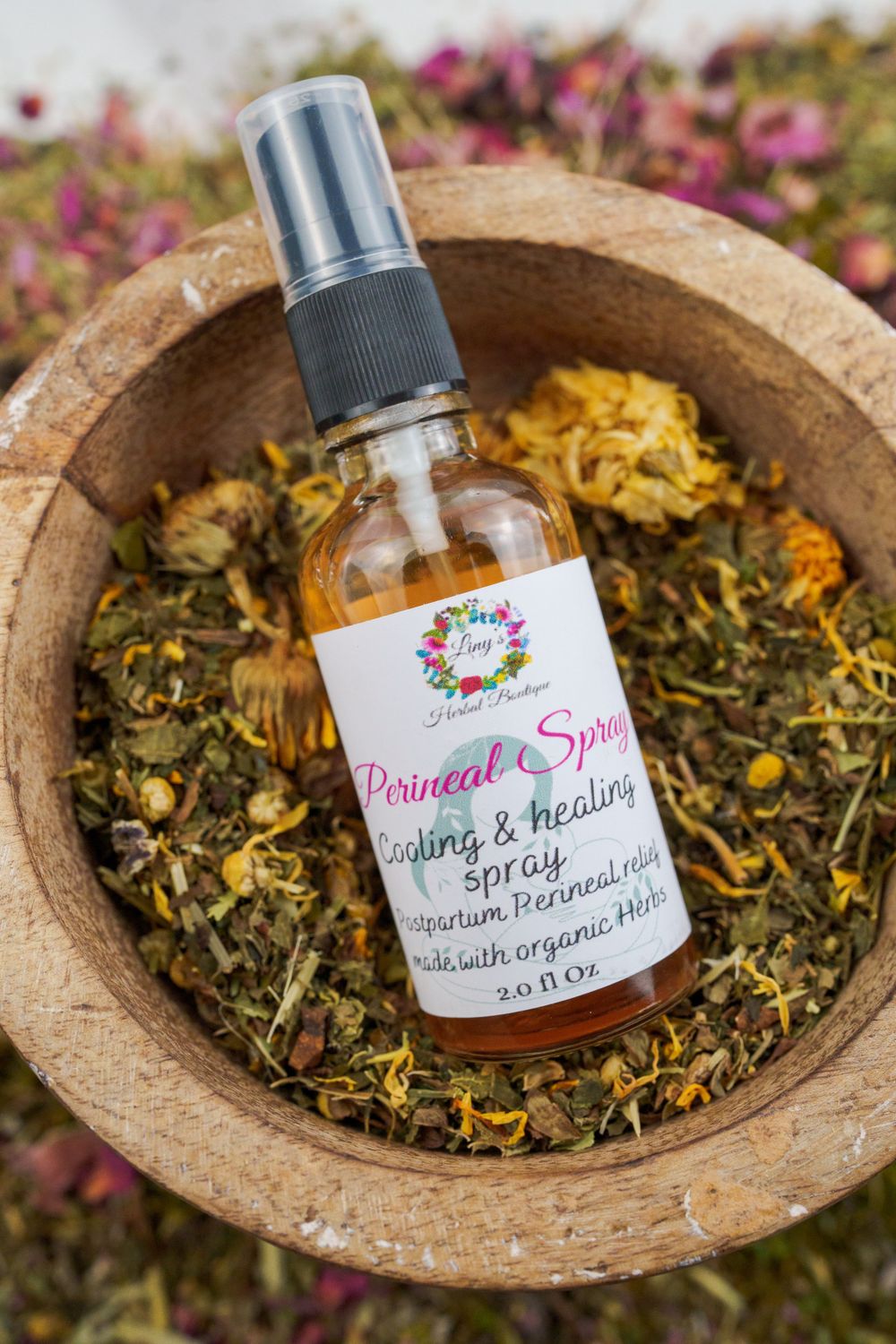 Herbal spray bottle nestled in wooden bowl filled with dried botanical ingredients.