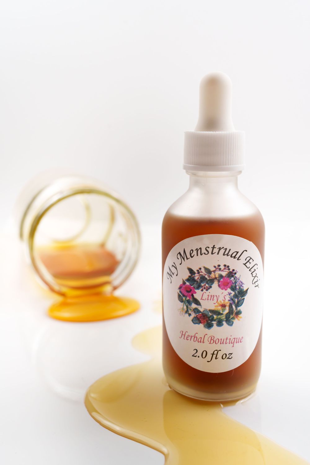 Herbal tincture bottle with dropper next to spilled golden liquid on white surface.
